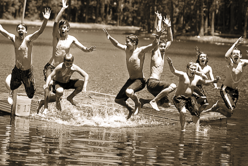 Group of kids jumping off a dock into a lake at summer camp