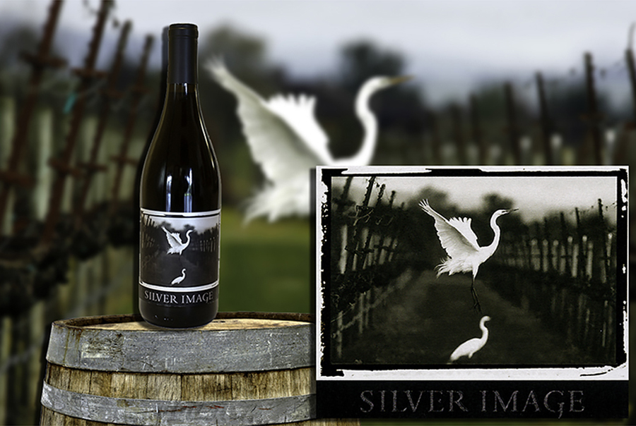 Silver image wine bottle on a barrel with picture of a white egret in the background and wine label superimposed